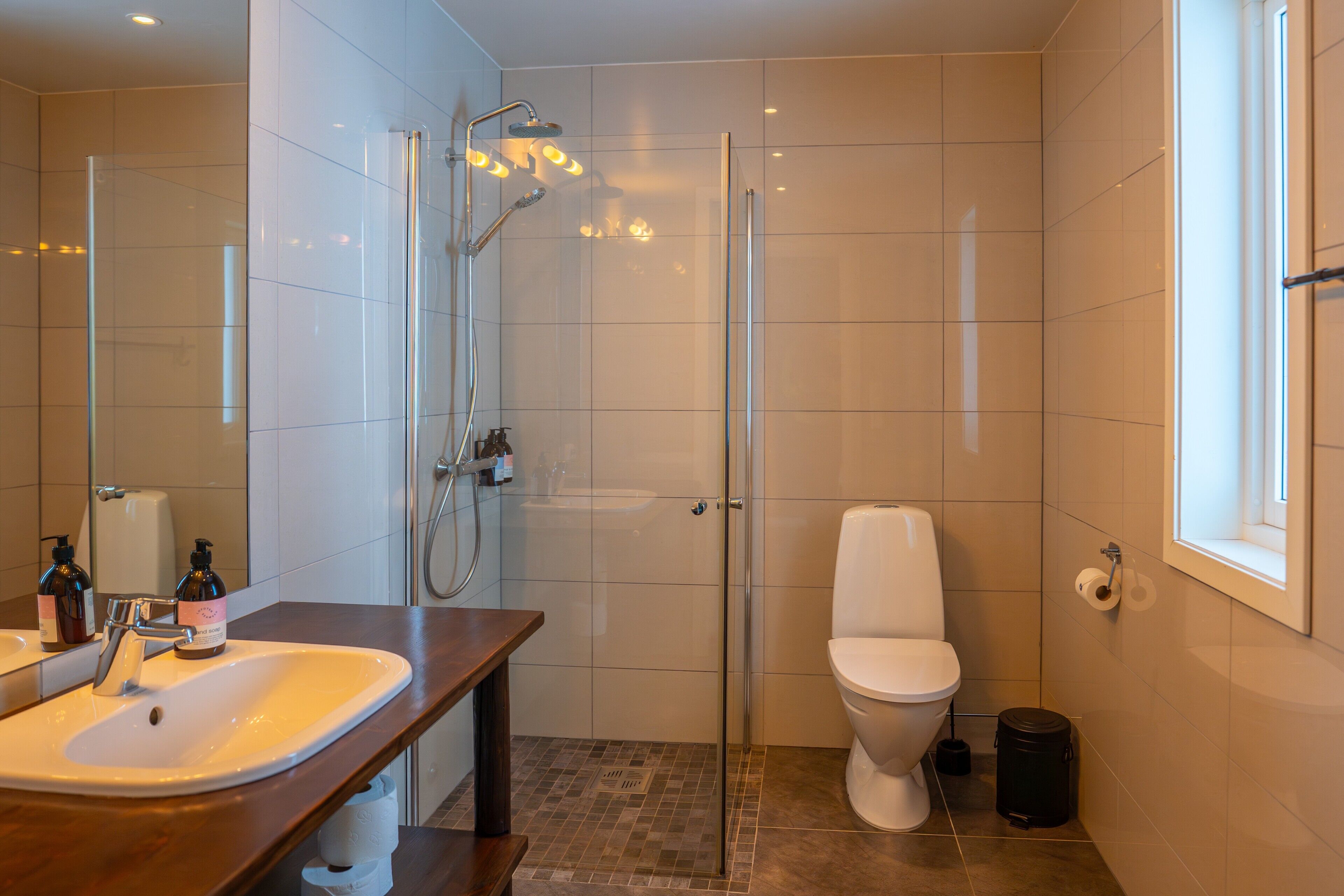 Une salle de bain moderne avec une douche à parois de verre, des toilettes blanches et un meuble-lavabo en bois avec un évier.