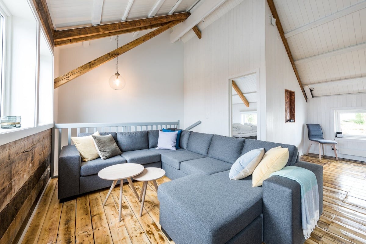 A modern living room with a large sectional sofa, two round side tables, and a wooden floor.