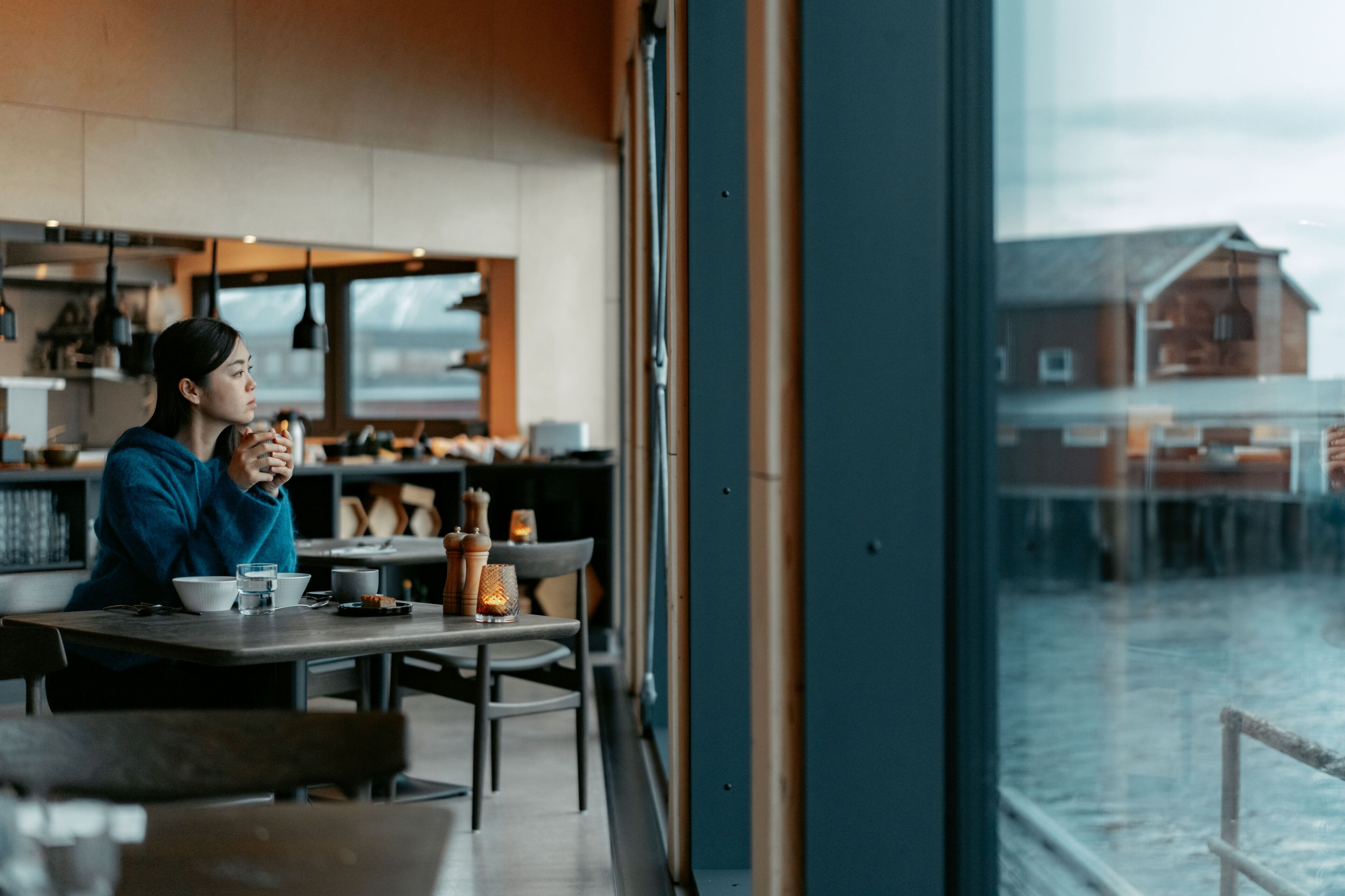 A person sitting at a table in a modern cafe with a view of a building outside.