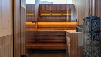 Una sauna con bancos de madera, pared de piedra y puerta de cristal.