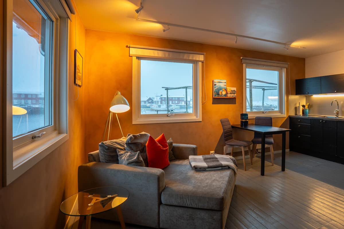 A modern living room with a sofa, a small table, and a view of the city through large windows.