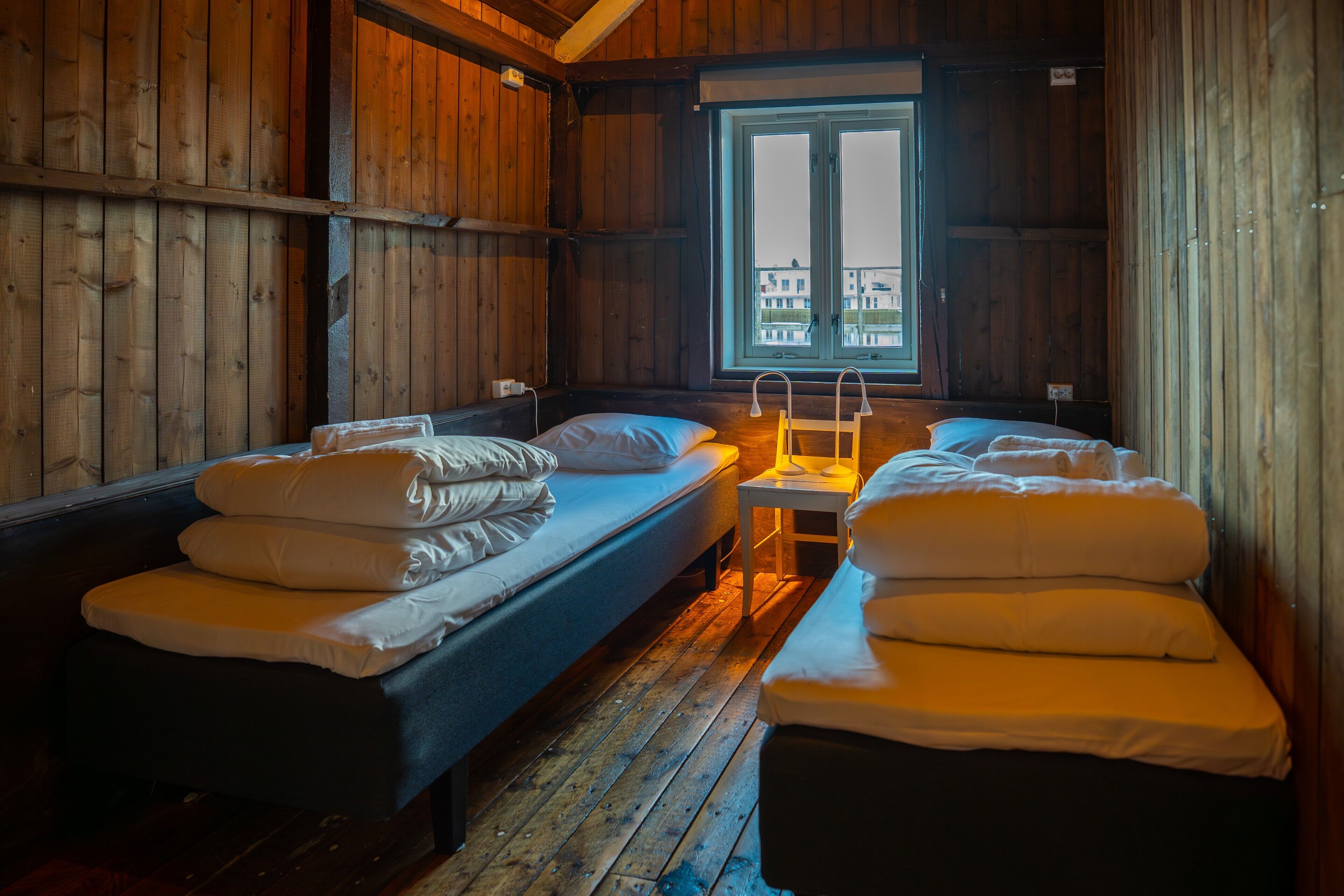 A cabin with two single beds, a small table, and a window with a view of buildings.