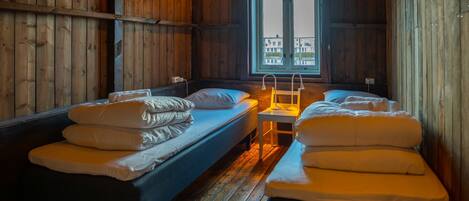 A cabin with two single beds, a small table, and a window with a view of buildings.