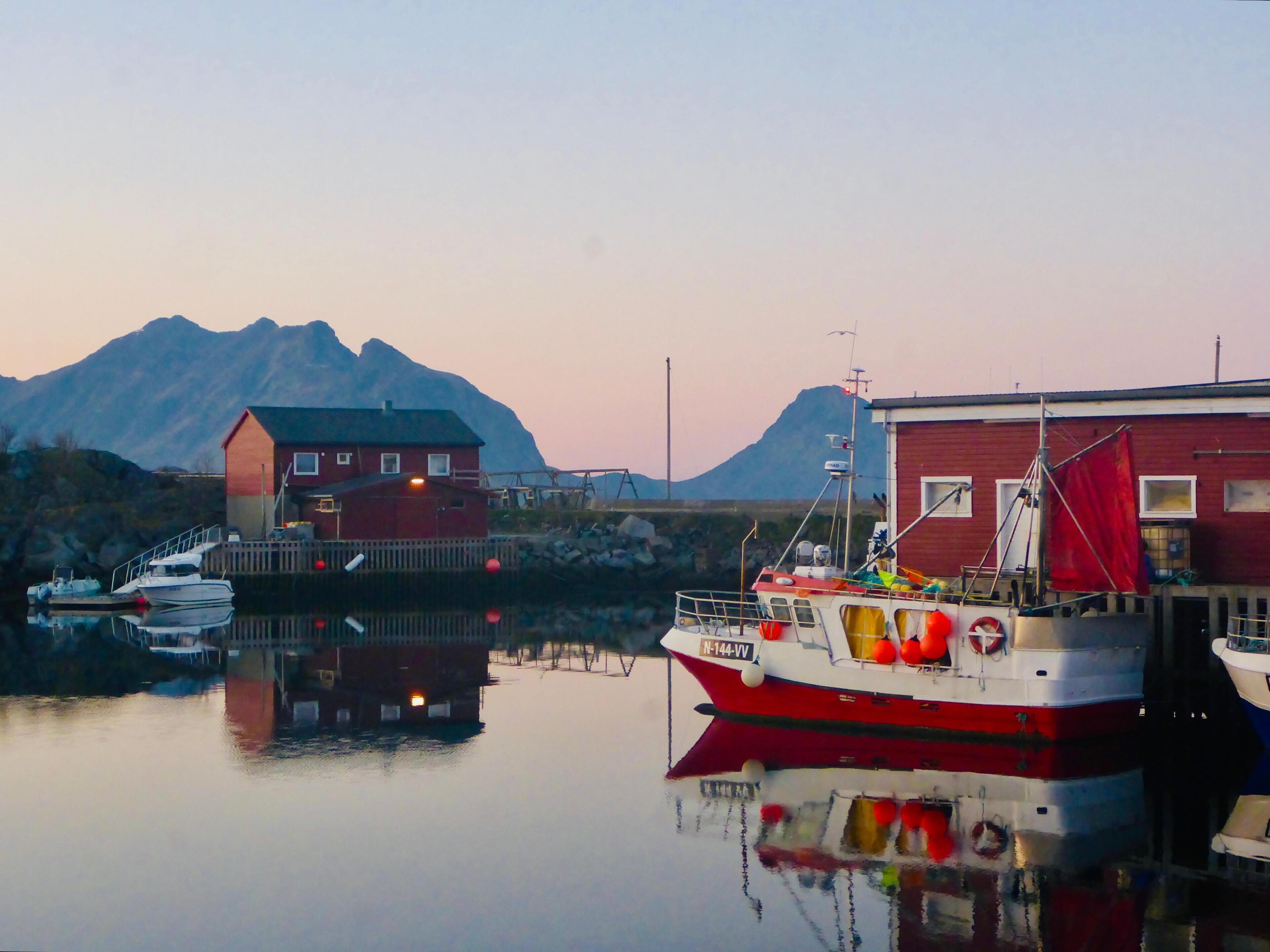 A harbor with boats, a wooden dock, and a red building with a white window.