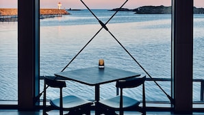 A table with two chairs facing a view of the sea, a lighthouse, and rocky outcrops. - Hattvika Lodge (Vestvagoy)