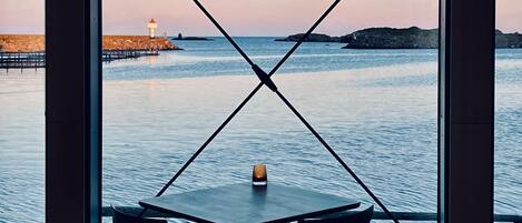 A table with two chairs facing a view of the sea, a lighthouse, and rocky outcrops.