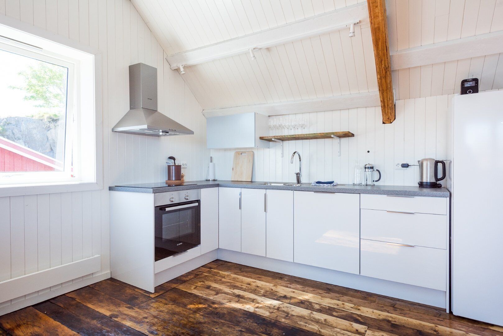 Een moderne keuken met witte kasten, een ingebouwde oven, een roestvrijstalen afzuigkap, een houten aanrechtblad en een raam dat natuurlijk licht binnenlaat.