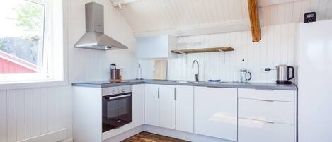 Una cocina moderna con armarios blancos, horno empotrado, campana extractora de acero inoxidable, encimera de madera y ventana que deja entrar luz natural.