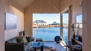 Un intérieur moderne avec un canapé, une table basse et une vue sur le bord de l’eau, avec des bâtiments et des montagnes en arrière-plan.