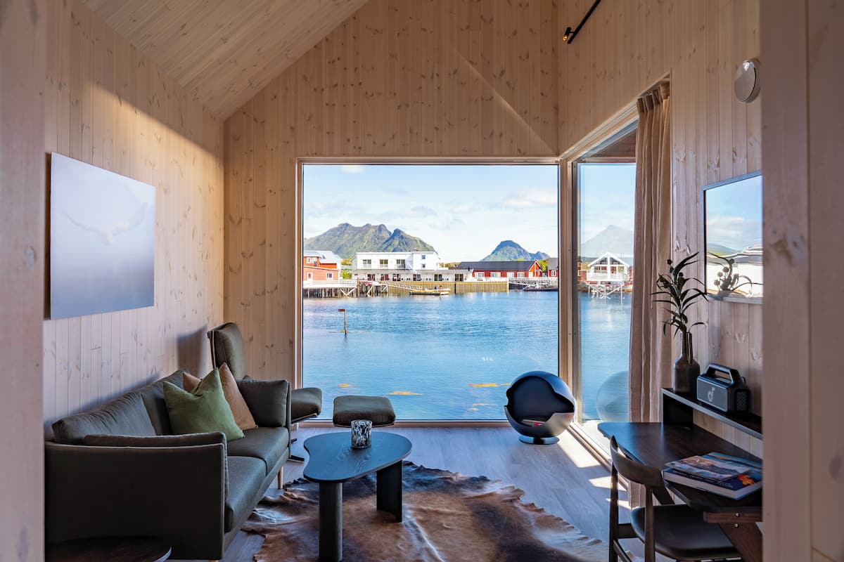 A modern interior with a sofa, coffee table, and a view of a waterfront with buildings and mountains.