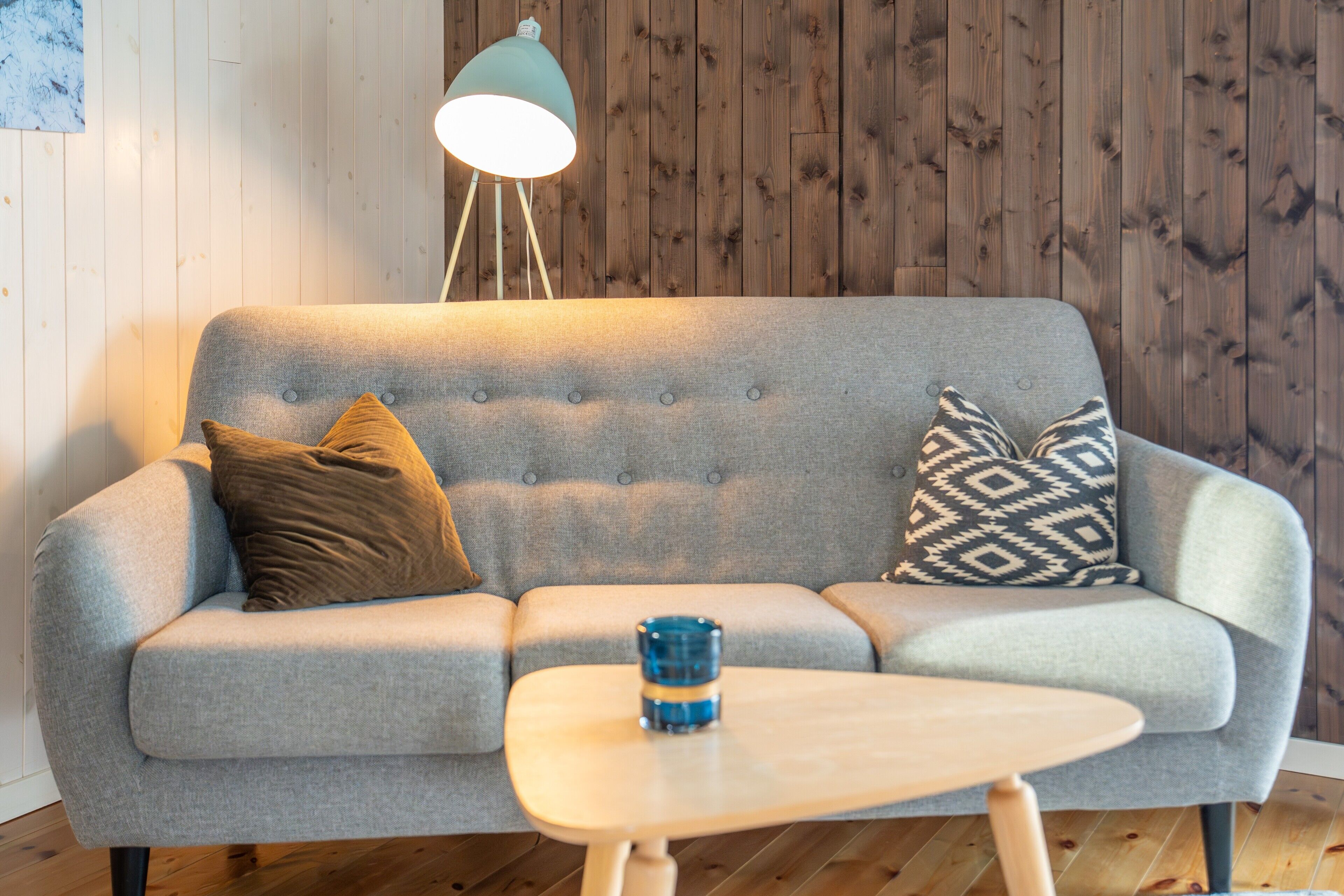A grey sofa with two patterned cushions, a small wooden table, and a floor lamp.
