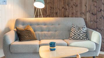 A grey sofa with two patterned cushions, a small wooden table, and a floor lamp.