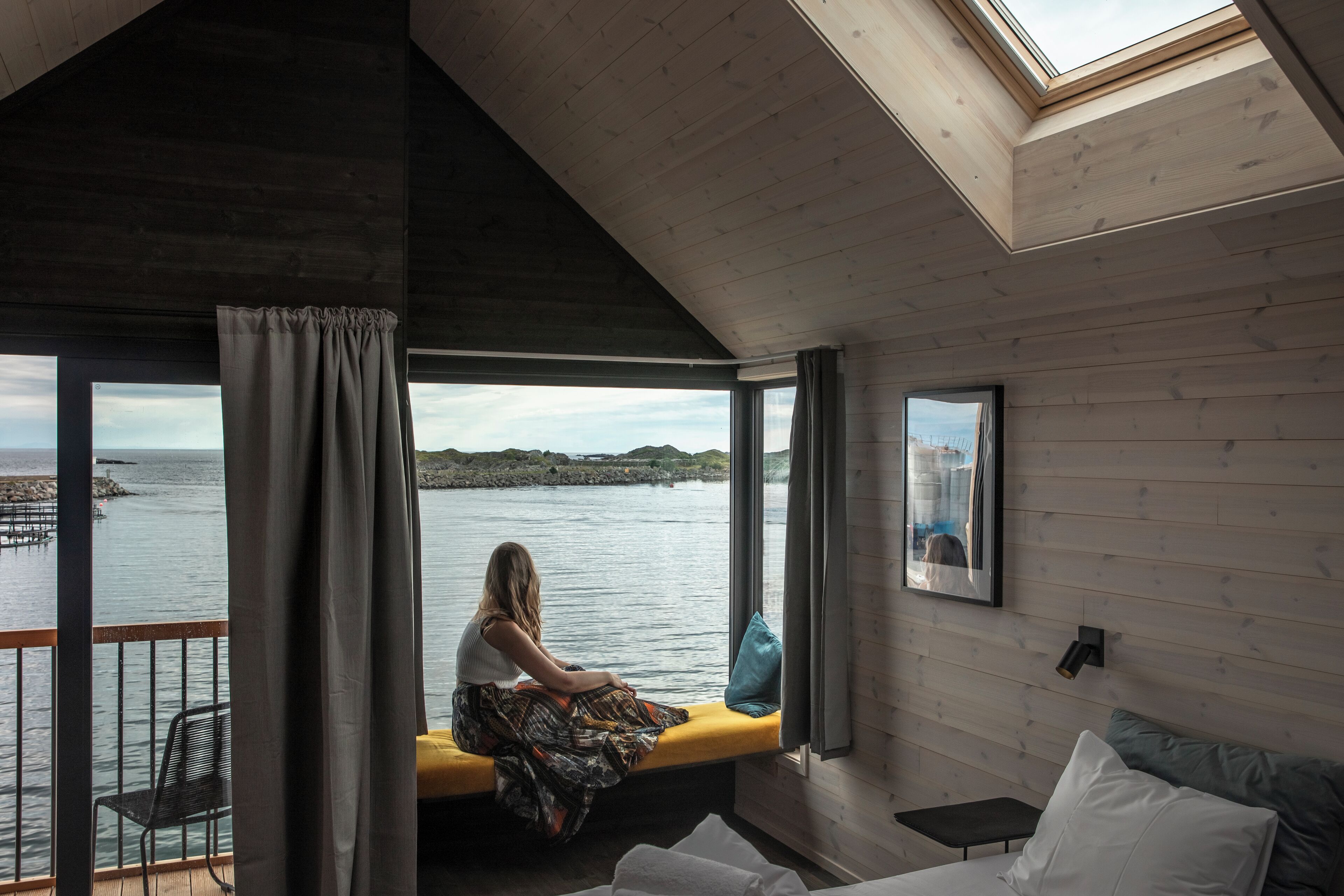 A room with a view of the water, a bench, a bed, and a skylight.