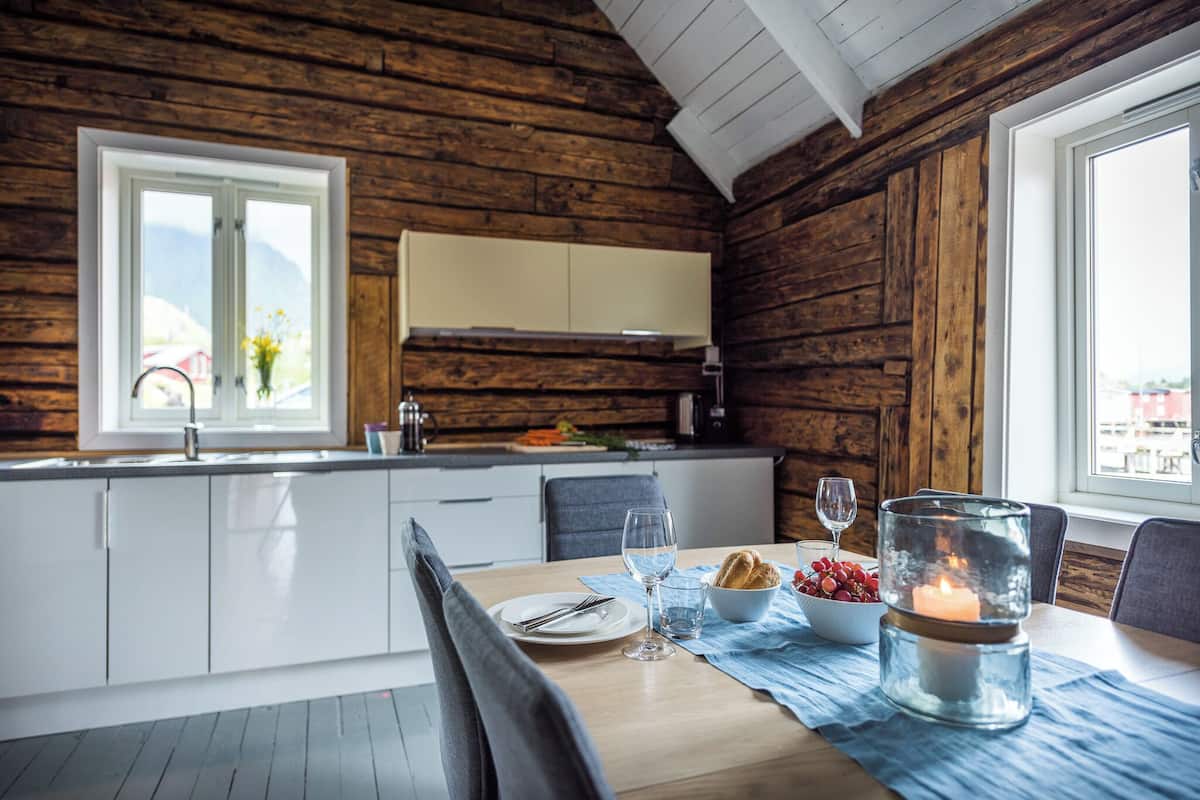 A wooden cabin interior with a dining table set for two, a candle, and a bowl of fruit.