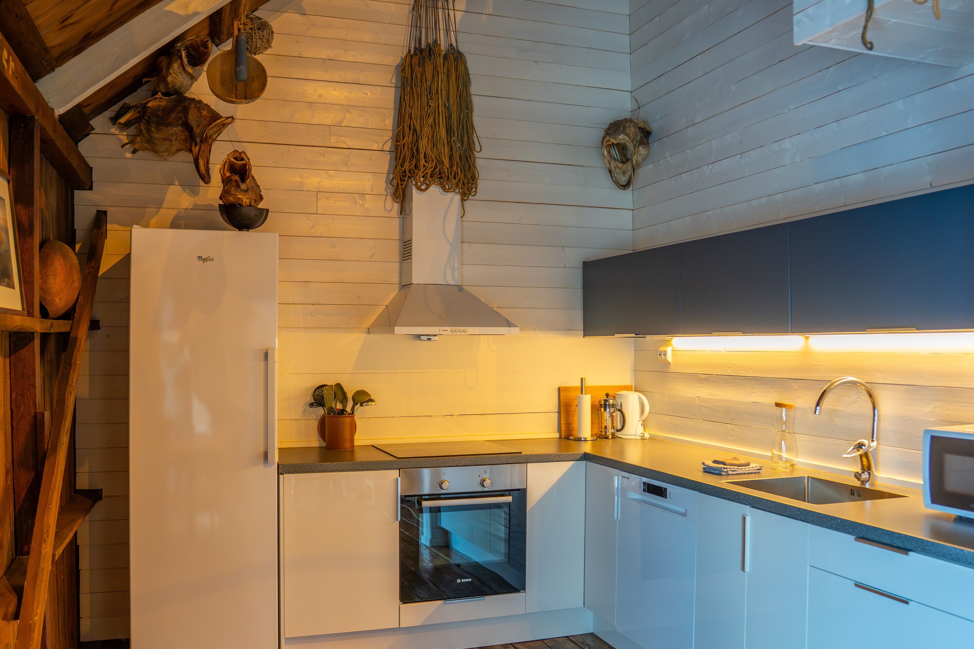 A modern kitchen with white cabinetry, a built-in oven, a stainless steel sink, and a hanging light fixture.