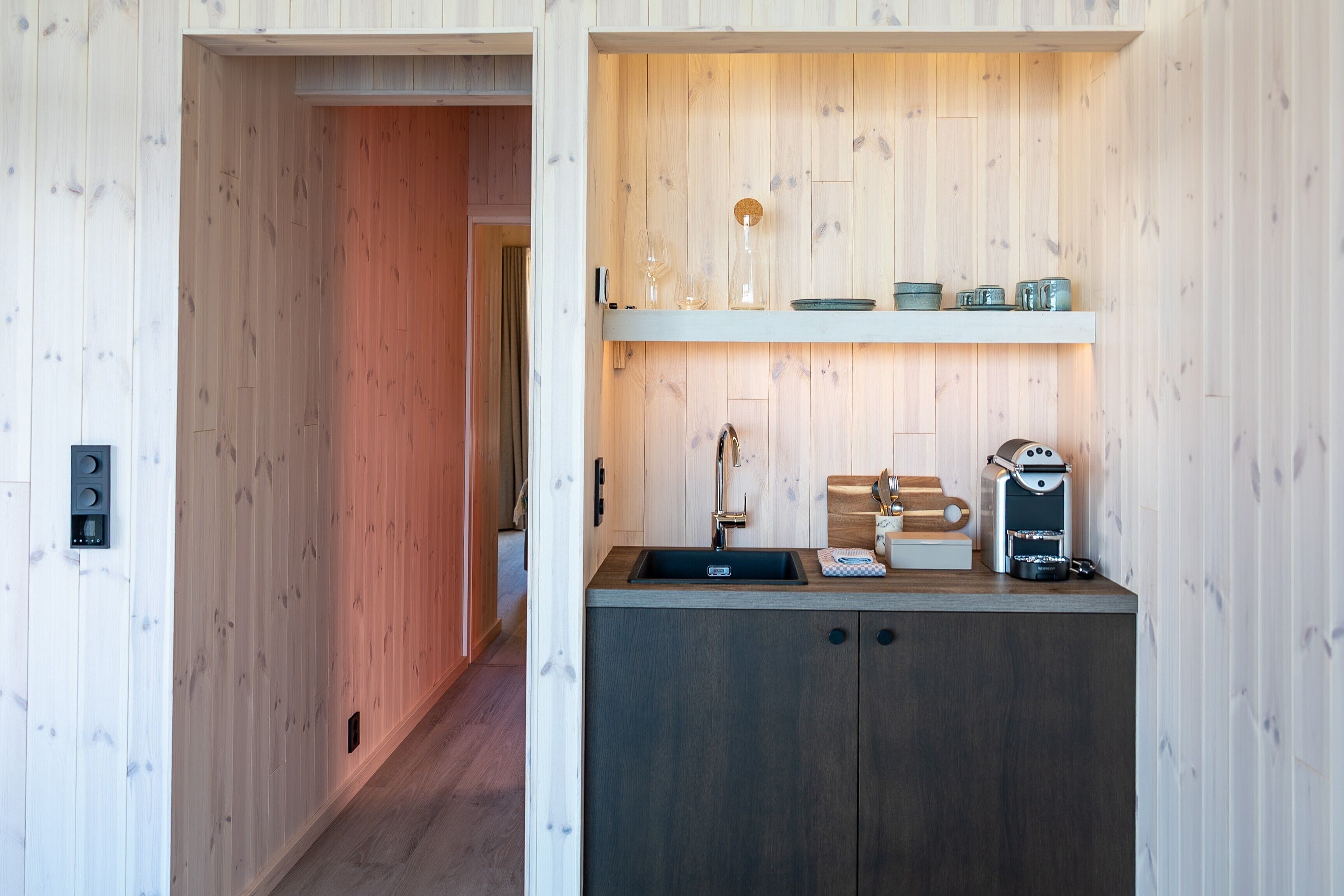 A compact kitchen with a built-in sink, wooden cabinets, and a coffee machine.