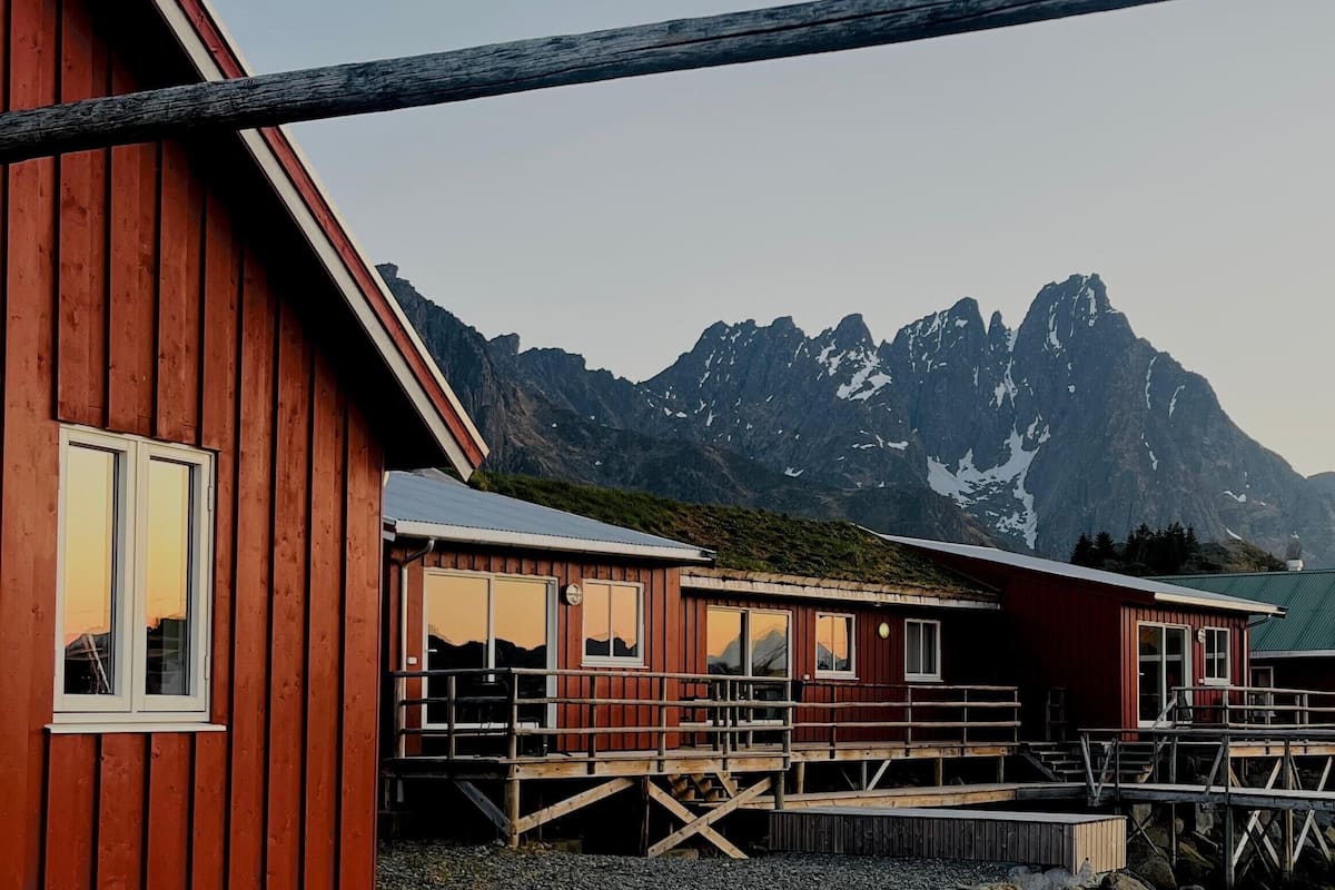 A wooden cabin with a deck, large windows, and a mountain backdrop.