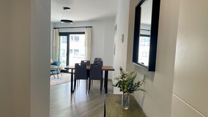 Ein Flur, der in einen Essbereich mit Tisch und Stühlen führt, eine Vase mit Blumen auf einem kleinen Tisch und ein großer Spiegel an der Wand.