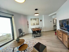 A modern living room with a dining area, a TV, and a large window. - Enjoy the Estepona sunshine in a modern apartment close  to the center and beach (Estepona)