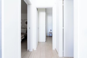 Ein Flur mit weißen Wänden und Türen, die zu einem Schlafzimmer und einer kleinen Schreibtischzeile führen.