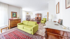 Una sala de estar con un sofá verde, un armario de madera y una zona de comedor con sillas y una mesa.