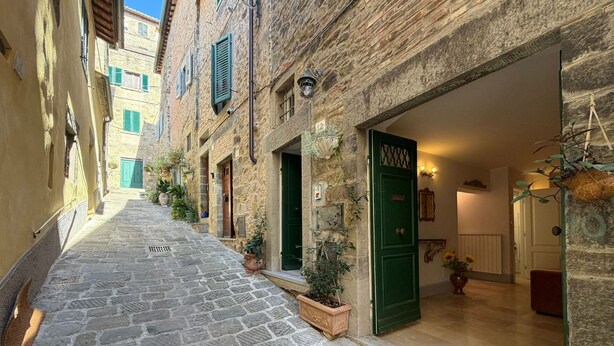 A narrow cobblestone street with stone buildings, green doors, and potted plants. - Lovely apartment for 2 guests with WIFI, A/C and TV (Cortona)