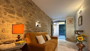 A cozy living room with a stone wall, a brown sofa, a small table with a lamp, and a vase with sunflowers. - Lovely apartment for 2 guests with WIFI, A/C and TV (Cortona)