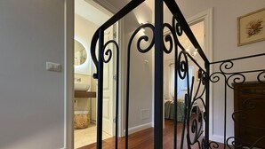 A wooden staircase with black metal railings leading to a room with a white door, a mirror, and a chandelier. - Lovely apartment for 2 guests with WIFI, A/C and TV (Cortona)