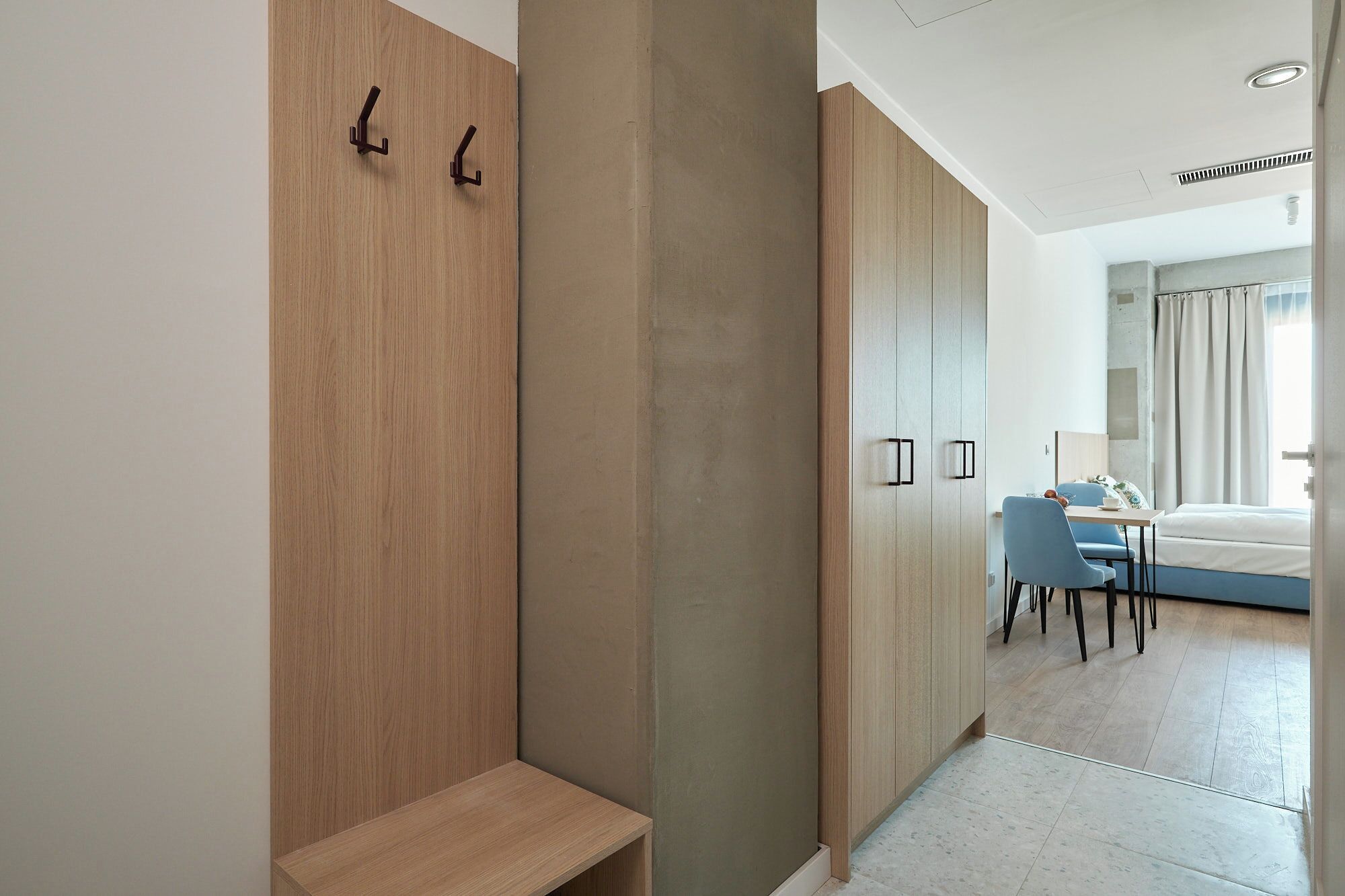 Une chambre d’hôtel moderne, dotée d’une armoire en bois, d’un banc, d’un coin repas avec une table et des chaises, et offrant une vue sur l’extérieur.