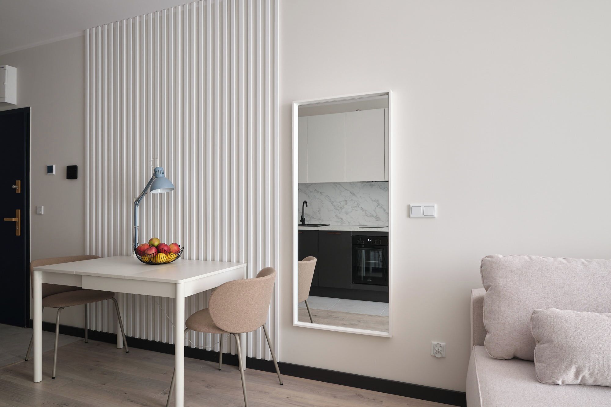 Un salon moderne avec un canapé blanc, un coin repas comprenant une table et des chaises, une cuisine visible à travers une fenêtre et un radiateur.