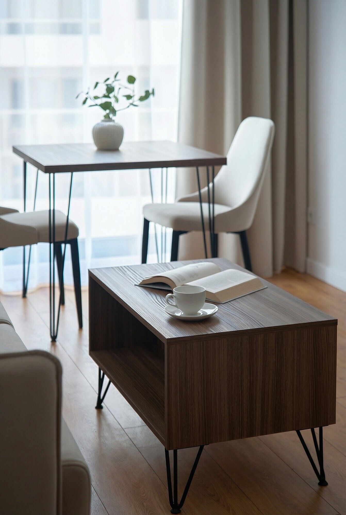 A modern room with a wooden coffee table, a white chair, and a table with a potted plant.
