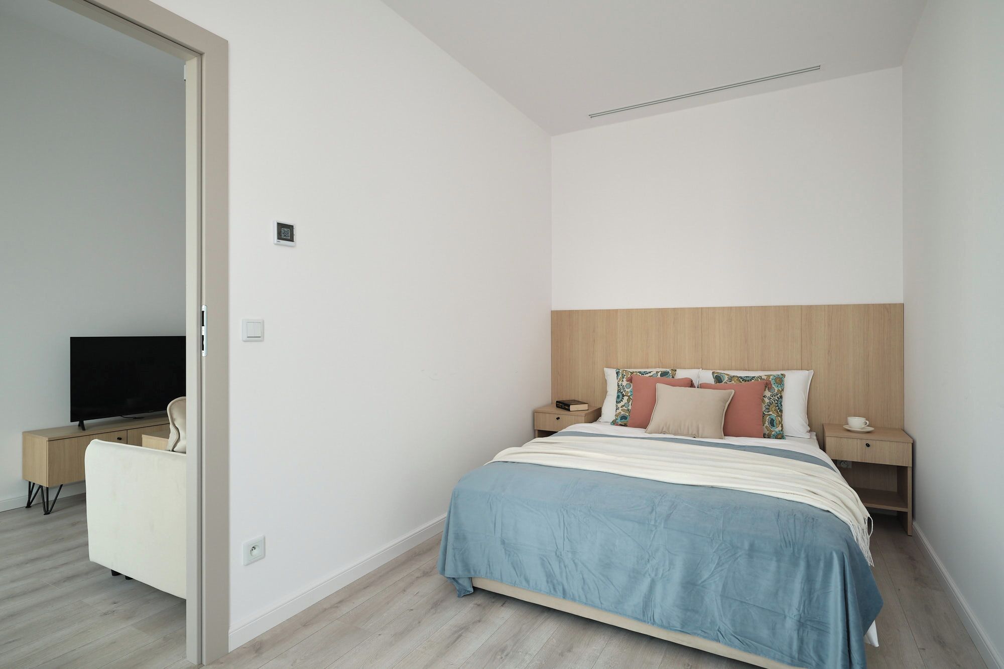 Une chambre à coucher avec un lit, des tables de chevet, une télévision et une porte.