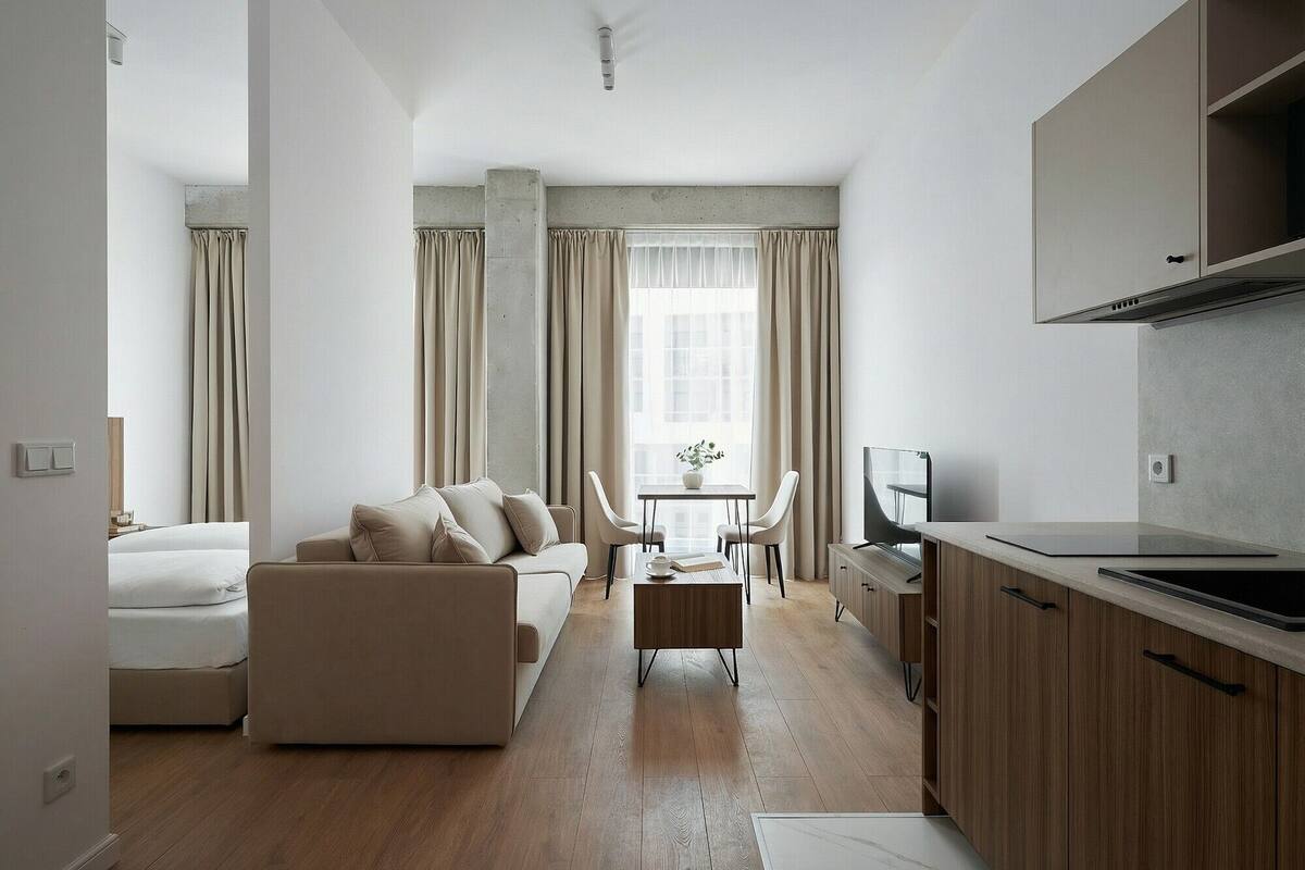 Un salon moderne comprenant un canapé, un coin repas avec des chaises, une petite table, et un espace cuisine avec des placards et un plan de travail.