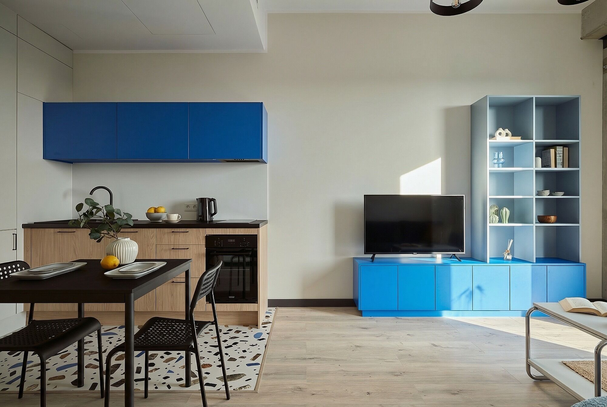 Una cocina moderna con armarios azules, un comedor con mesa y sillas, un televisor de pantalla plana y una estantería.