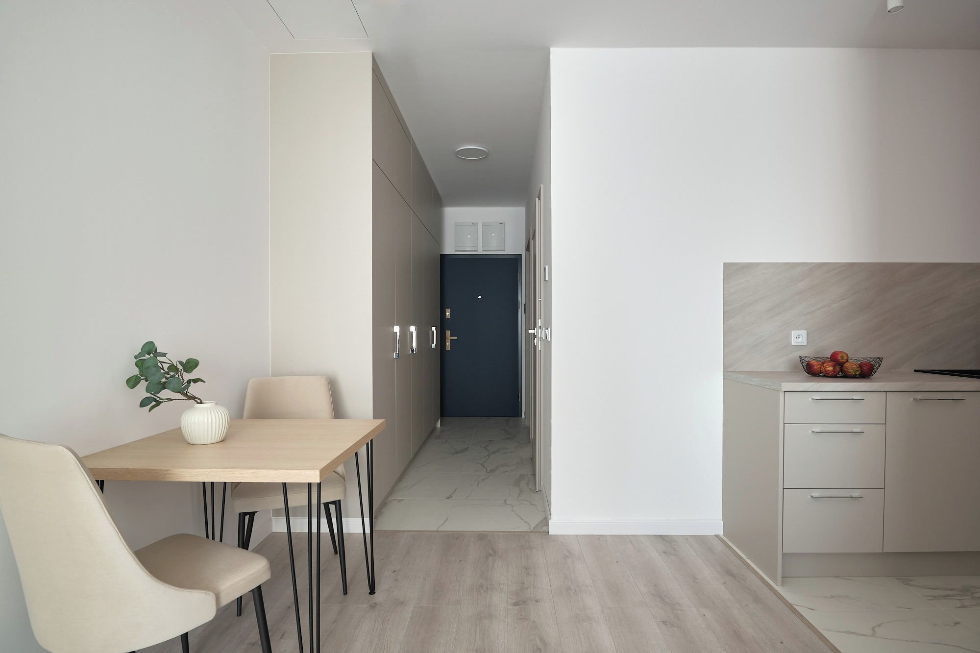 Una cocina moderna con encimera de mármol, un comedor con mesa y sillas, y un pasillo que lleva a una puerta.