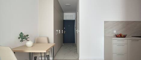 Una cocina moderna con encimera de mármol, un comedor con mesa y sillas, y un pasillo que lleva a una puerta.