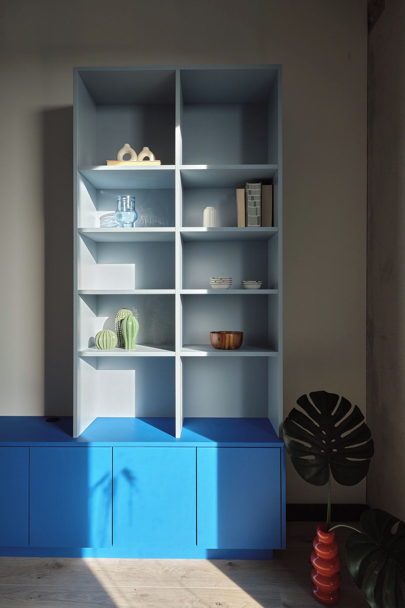 Ein Zimmer mit einem blauen Schrank, einem weißen Regal und einer Pflanze.
