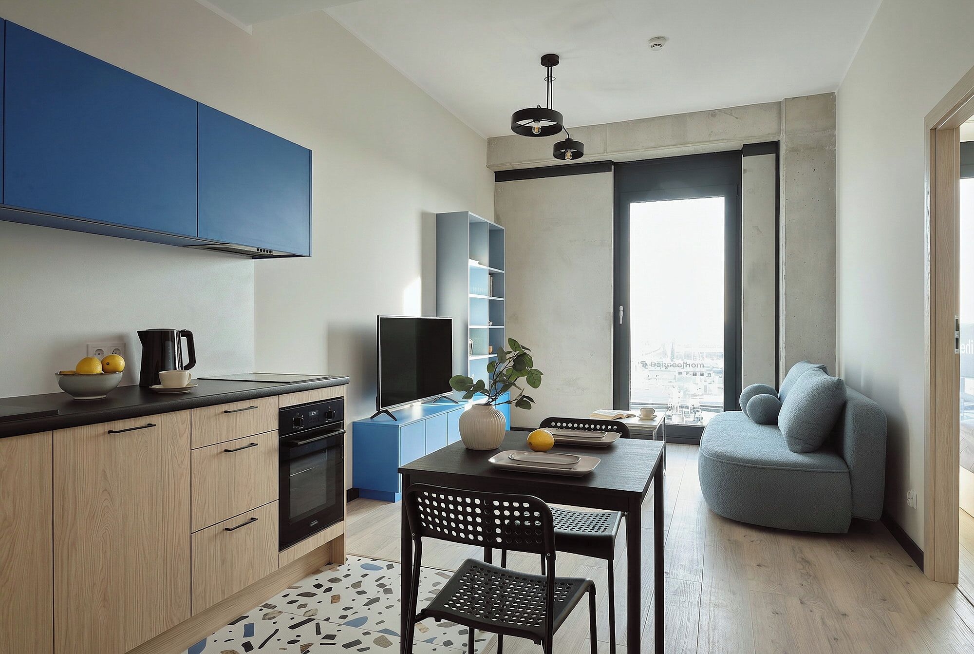 A compact kitchen with modern appliances, a dining area with a table and chairs, and a view through a large window.