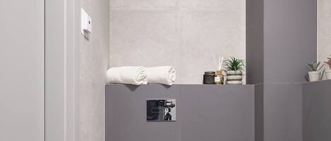 A modern bathroom with a toilet, a towel, and a small shelf with toiletries.