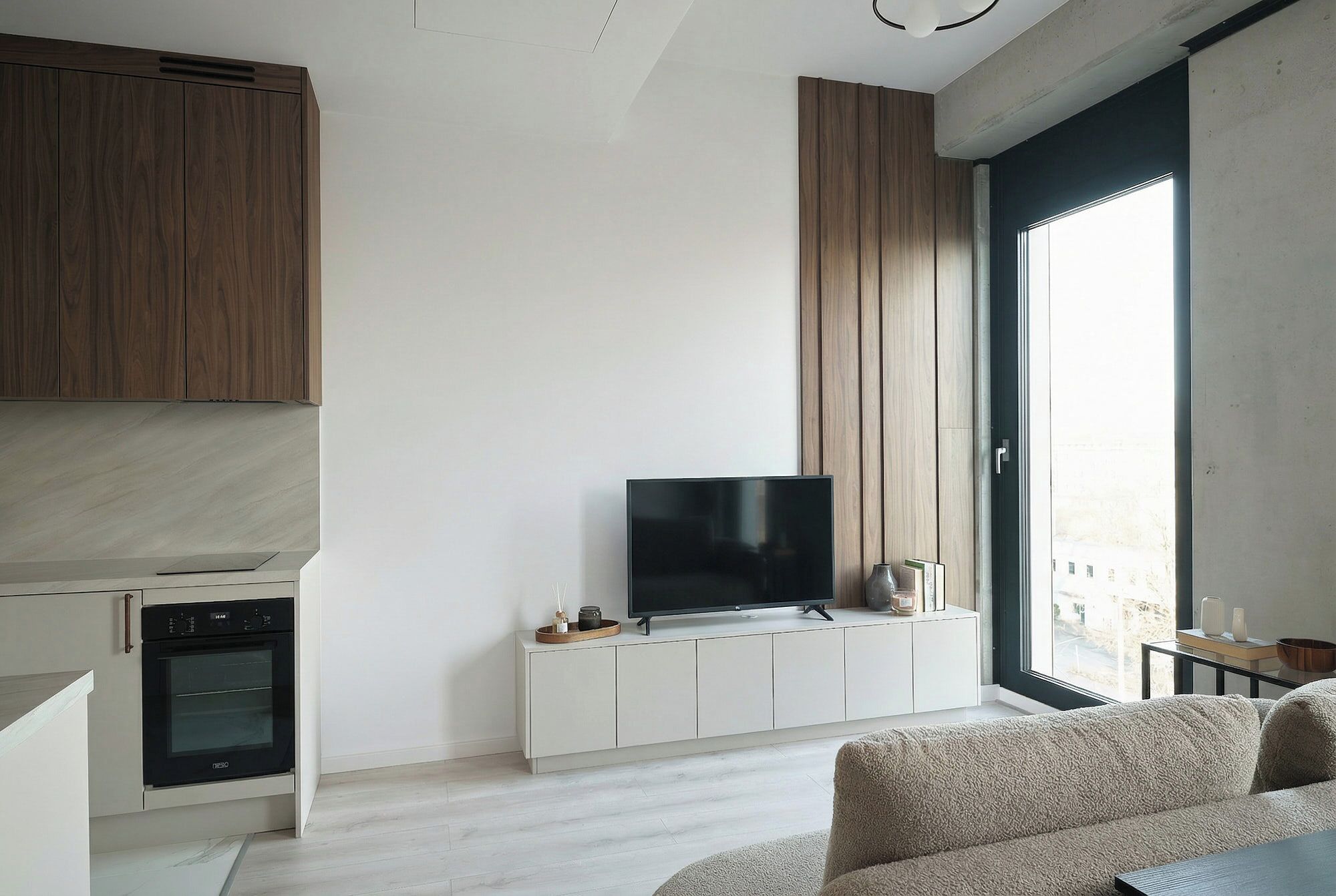 Una cocina moderna con horno empotrado, un televisor sobre un mueble blanco y un amplio ventanal con vistas.