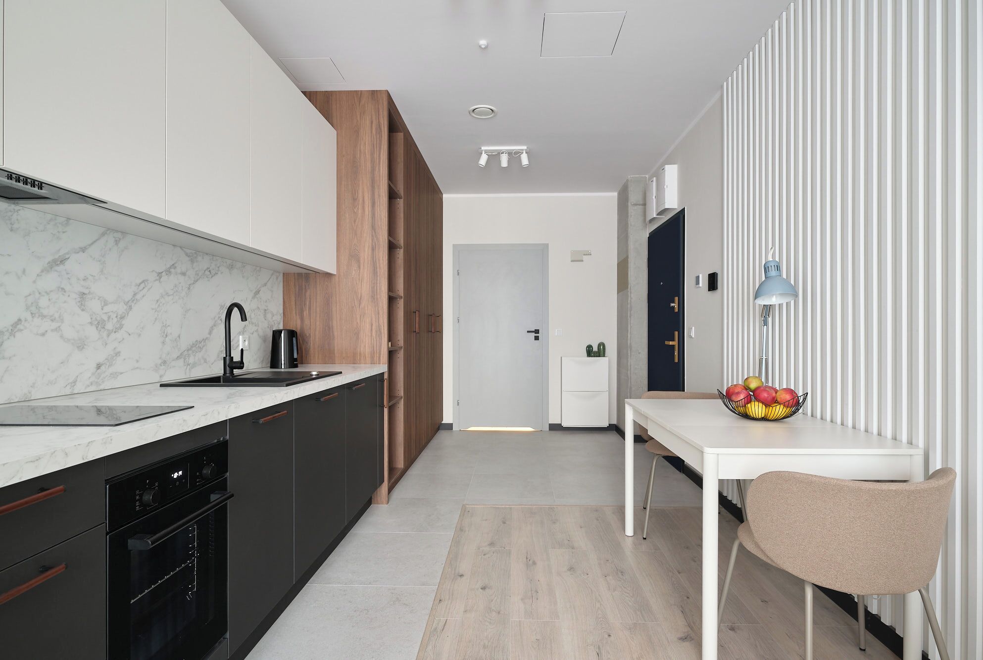 A modern kitchen with dark cabinetry, a marble countertop, and a wooden accent wall.