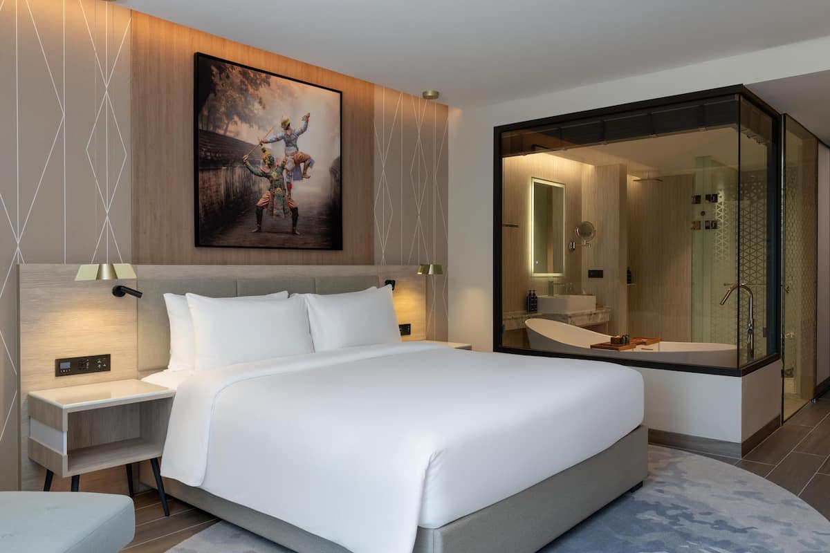 Una habitación de hotel moderna con una cama grande, una mesita de noche, un escritorio, una ducha con mampara de cristal y un cuadro en la pared.
