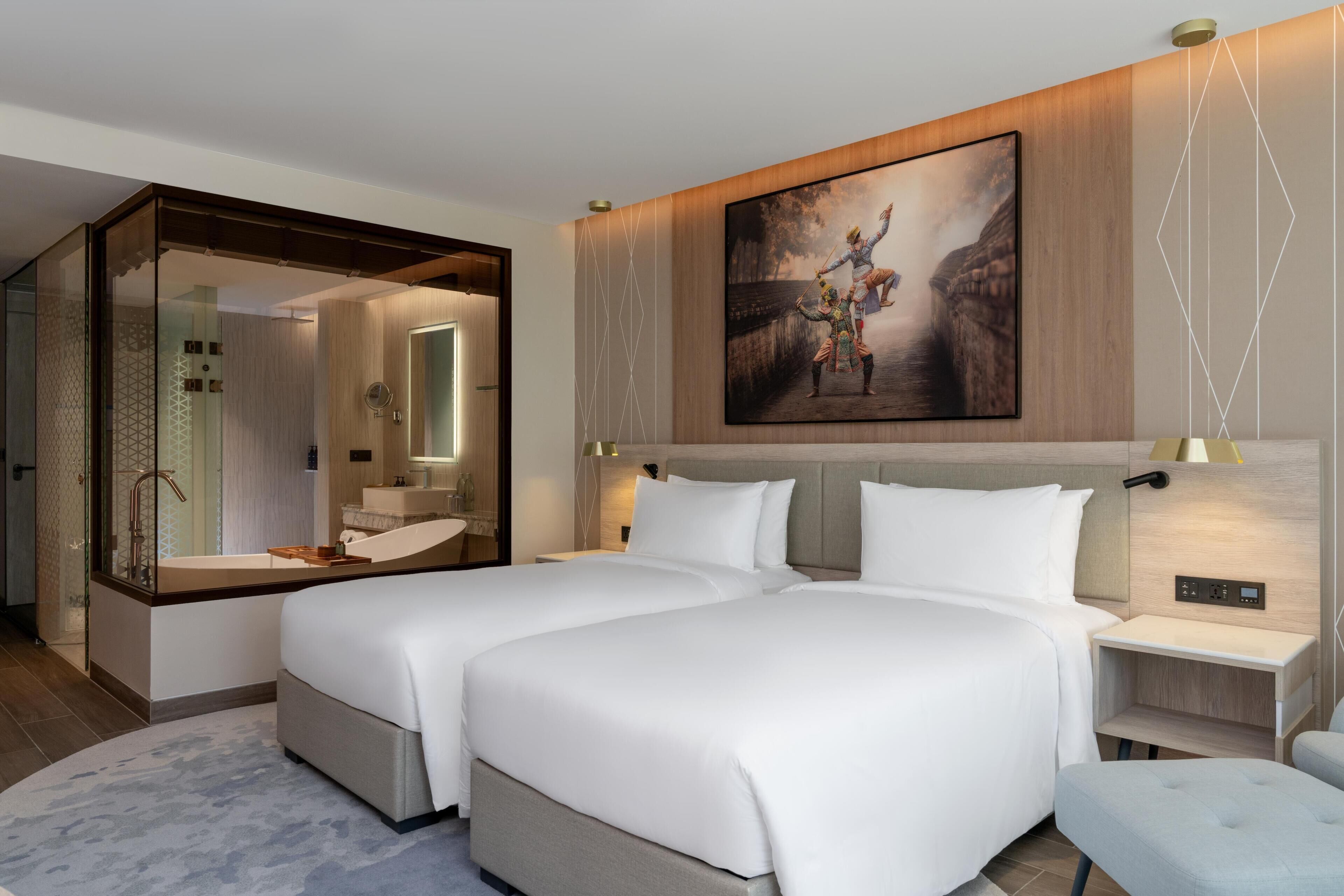 Une chambre d’hôtel moderne avec deux lits, un grand miroir, un tableau et une salle de bain dotée d’une paroi en verre.