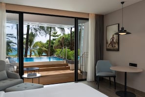 Une chambre d’hôtel moderne dotée d’une grande porte-fenêtre coulissante donnant sur un espace piscine, d’un lit, d’une petite table et d’une chaise.