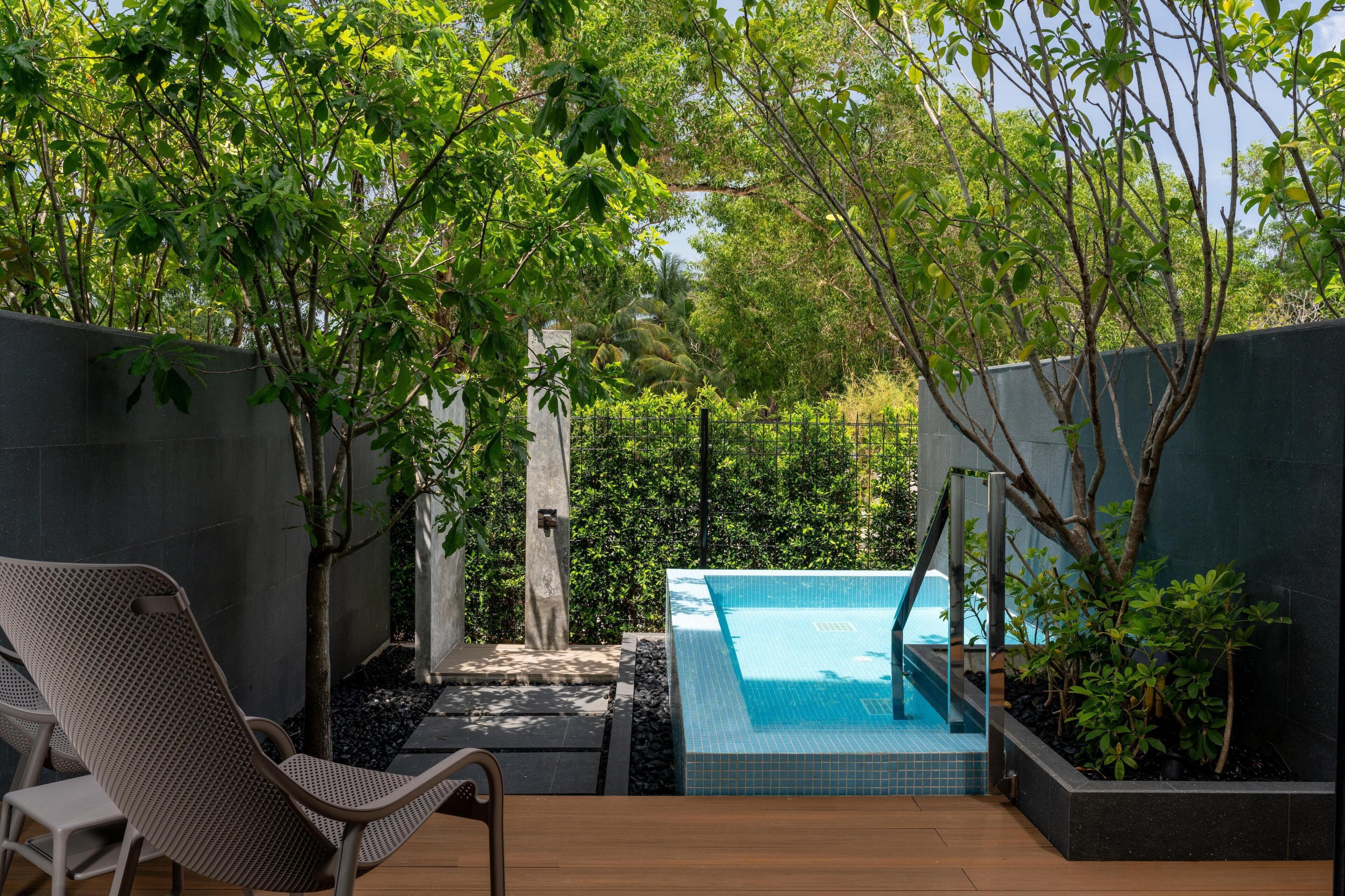 A pool area with a wooden deck, a lounge chair, and a small garden with a fence.