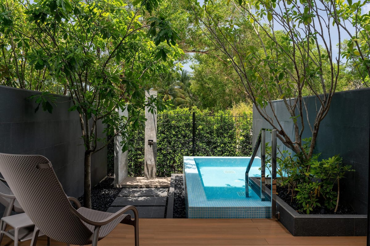 Una zona de piscina con un muelle de madera, una silla de descanso y un pequeño jardín con valla.