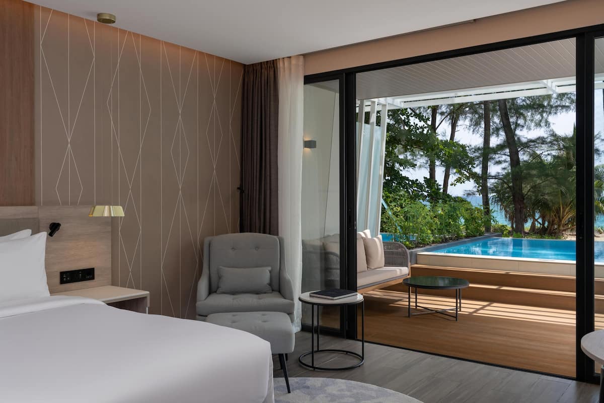 Una habitación de hotel moderna con una cama, una silla, una mesita, un sofá y vistas a una piscina al aire libre.