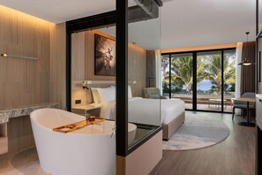 A modern hotel room with a large bathtub, a bed, a desk, and a balcony with a view of palm trees.