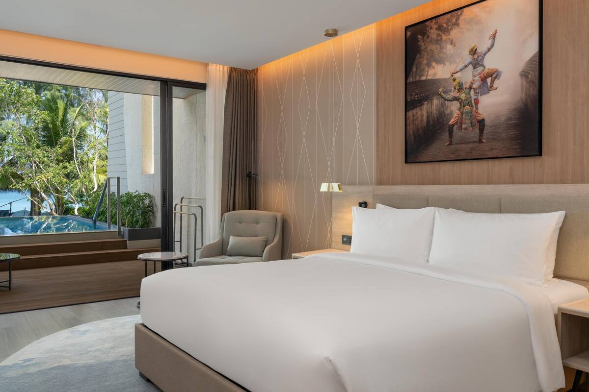 Una habitación de hotel con una cama grande, una silla, una mesita y un cuadro en la pared.
