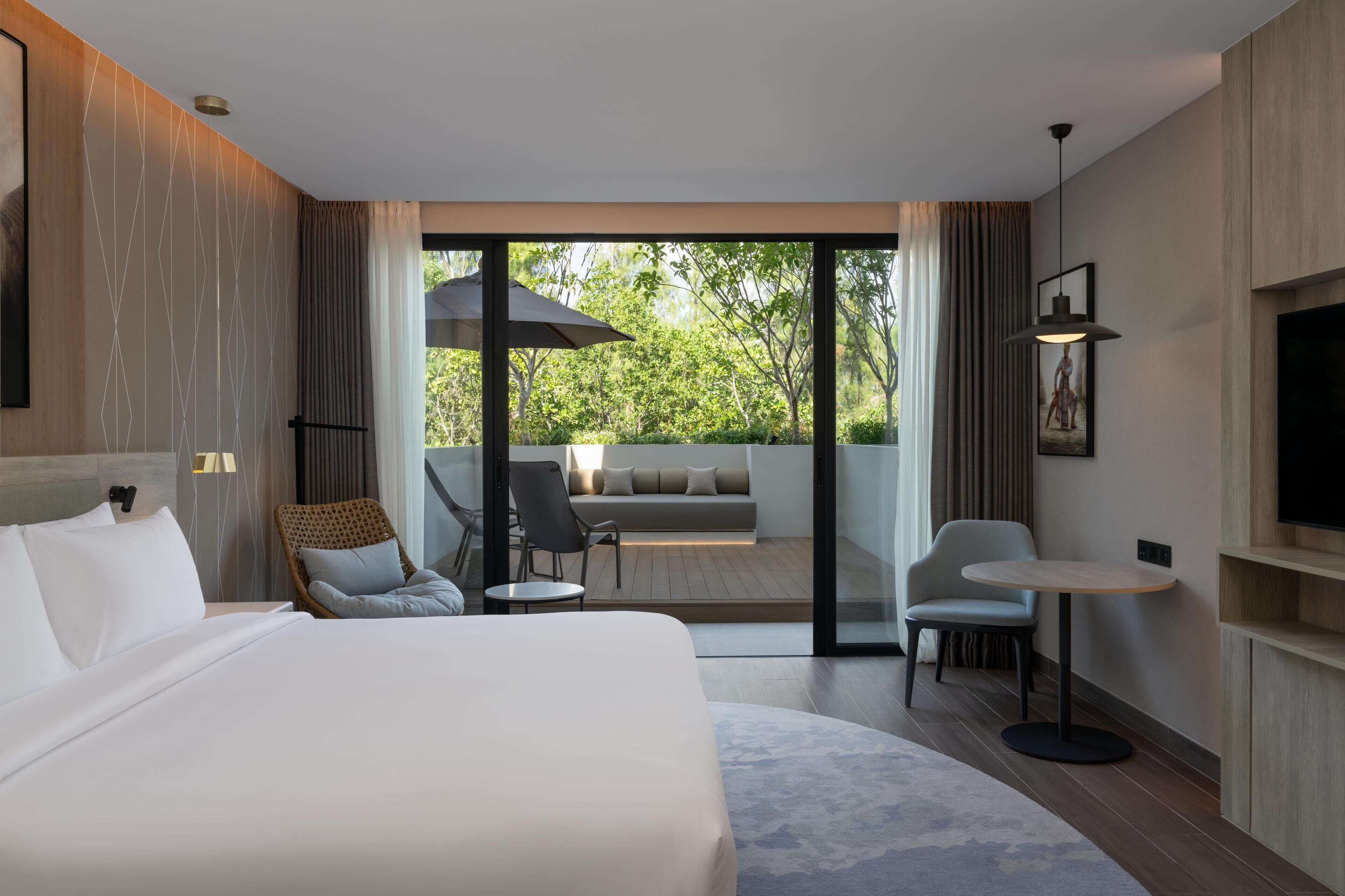 A modern hotel room with a large bed, a seating area with a sofa and chairs, a small table, and a TV.